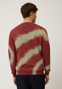 Rood en groen tie-dye sweatshirt met lange mouwen, voorzien van een ronde hals en geribde manchetten, van achteren getoond op een persoon.