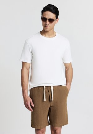 T-shirt blanc à manches courtes avec une finition texturée, associé à un short marron texturé avec une taille élastique et un cordon de serrage.