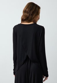 Zwarte lange mouwtop met een drapering aan de achterkant en een zachte textuur. De ronde hals en aansluitende mouwen passen mooi bij de vloeiende silhouet.
