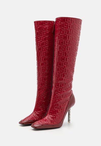 Sarkans ceļgalu augumā botas ar glancētu virsmu, iespiedotu logotipa rakstu, smailu purngalu un augstu stiletto papēdi ar dekoratīvu akcentu.