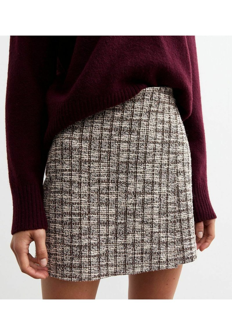 Tweed mini-jurk met een patroon in roomwit en donkerbruin, met verticale strepen. Gepaard met een bordeauxrode trui.