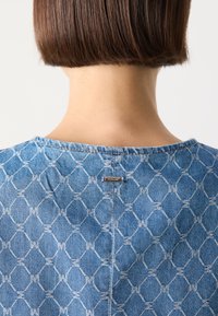 Denim gornji dio u svijetloplavoj boji s geometrijskim uzorkom. Osvijetljen malom metalnom etiketom sa nazivom brenda smještenom blizu izreza.