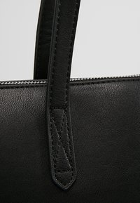 Černá kožená kabelka s texturovaným povrchem, obsahující výrazný šev na uchu a stříbrný zip podél horního okraje.