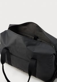 Μαύρη υφασμάτινη τσάντα σκληρής κατασκευής με φερμουάρ, διαθέτει διπλούς χειρολαβές και εξωτερική τσέπη. Μαλακό υλικό με μίνιμαλ σχέδιο.