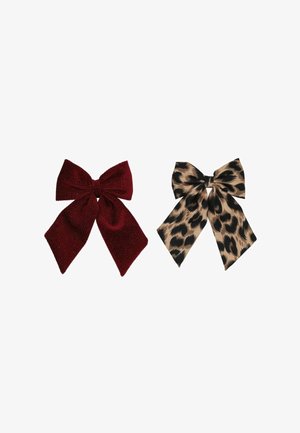 Deux nœuds décoratifs en tissu côte à côte, l’un rouge profond avec des paillettes, l’autre beige avec des taches de léopard noires.