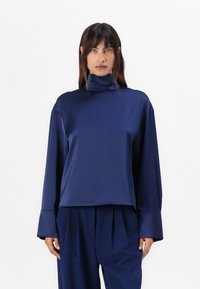 Maglione a collo alto di colore blu navy con maniche lunghe, realizzato in un materiale morbido e elasticizzato, caratterizzato da una vestibilità comoda e polsini larghi.