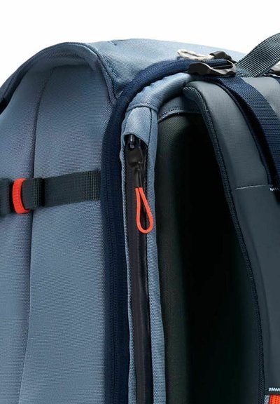 Mochila con un exterior azul y marino, tela texturizada, cremallera lateral con tirador naranja y compartimentos internos visibles.