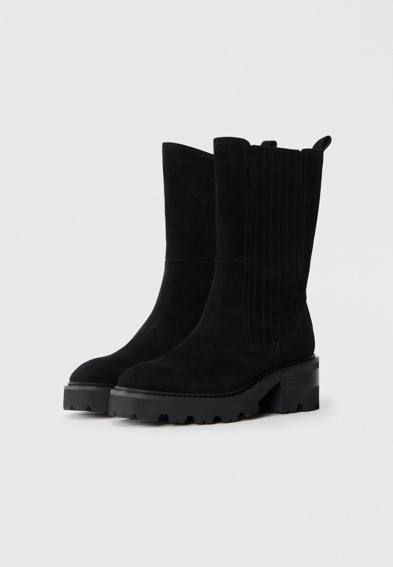 Botines de ante negro con un diseño estriado en los laterales, suela de goma gruesa y tacón bloque de altura media. Tirador delgado en la parte trasera.