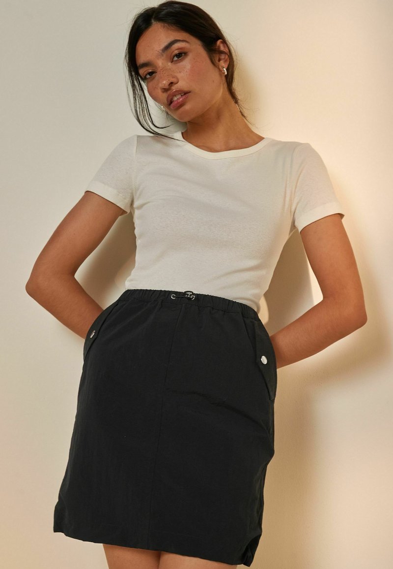 Haut blanc à manches courtes associé à une jupe noire jusqu'aux genoux avec une taille élastique et des poches latérales avec des fermetures à bouton.