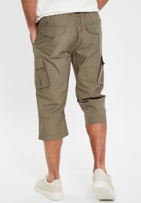Olijfgroene cargo shorts met een elastische tailleband, zijzakken en opgerolde boorden, gemaakt van een lichtgewicht stof, gedragen met lichtgekleurde sneakers.
