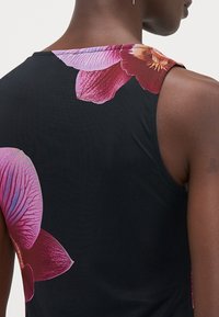 Débardeur noir avec de grands imprimés floraux d'orchidées roses et violettes sur les épaules, fabriqué dans un tissu doux et soyeux avec une coupe ajustée.