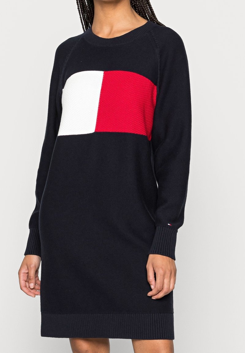 Robe pull en tricot bleu marine avec un panneau texturé rouge et blanc traversant la poitrine. Comprend un col rond ainsi que des poignets et un ourlet côtelés.