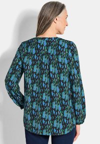 Langärmlige Bluse mit einem mehrfarbigen abstrakten Muster in Blau-, Grün- und Schwarztönen; leichtes Gewebe mit abgerundetem Saum.