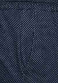 Námořnická tkanina s malými geometrickými modrými vzory; hladký povrch; obsahuje elastický pas a šev boční kapsy.