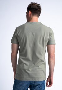 Camiseta de manga corta en verde olivo, de corte ajustado, fabricada con una suave mezcla de algodón de textura lisa. Etiqueta visible en el dobladillo.