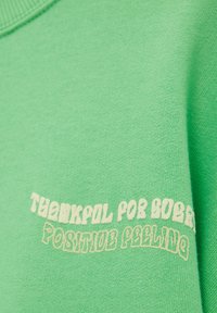 Tissu vert avec texte blanc disant « RECONNAISSANT POUR BOBBY » et « SENTIMENT POSITIF » en polices stylisées.
