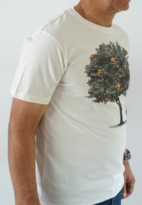 White cotton t-shirt featuring a graphic design of a leafy tree with burgers hanging as if they are fruit. Short sleeves and round neckline.