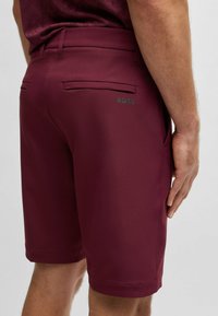 Burgundy cargo-shorts tillverkade av mjukt tyg, med slim fit, två bakfickor och en diskret grön logotyp på baksidan.