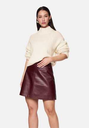 Cremiger Pullover mit gerippter Textur, hohem Kragen und lockeren Ärmeln. Burgunderfarbene Leder A-Linien-Rock mit Seitennähten und subtilen Hardware-Details.
