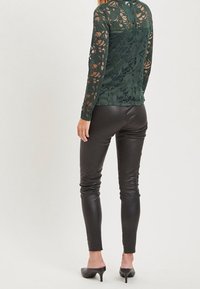 Top lungo a maniche con pizzo verde e motivi floreali, abbinato a pantaloni fittissimi in ecopelle nera. Il top presenta un design con schiena scoperta.