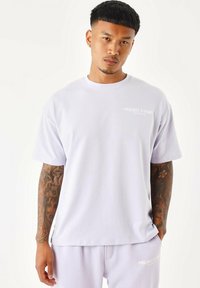 Camiseta de algodón de color púrpura claro con mangas cortas y cuello redondo. Presenta un pequeño logotipo blanco en el pecho y un corte holgado.