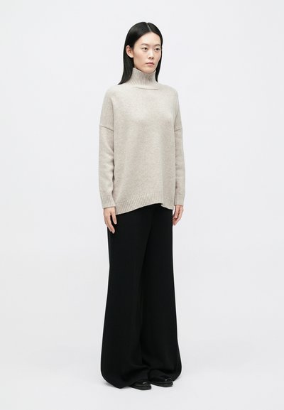 Φωτεινό μπεζ πουλόβερ με ψηλό λαιμό, άνετη εφαρμογή και ριμπ τελείωμα, συνδυασμένο με φαρδιά μαύρη παντελόνα. Ομαλή υφή, μινιμαλιστικός σχεδιασμός.