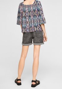 Lätt mönstrad blus med samlad krage, ihopparad med grå denimshorts med uppvikta muddar och bakfickor. Svarta sandaler.