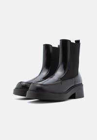 Μαύρες ankle μπότες με γυαλιστερή, πατίνα από δέρμα και ελαστικά πάνελ πλευρών, διαθέτοντας χοντρό τακούνι και πλατφόρμα.