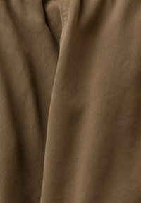 Ruskea teksturoitu kangas, jossa on vinonauhamainen kuvio, osoittaa taitettuja kerroksia, jotka korostavat pehmeyttä ja paksuutta.