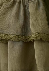 Tissu vert olive en couches avec une surface texturée et une bordure décorative au crochet le long du bord.