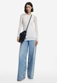 Top bianco a maniche lunghe con tessuto testurizzato, orlo a strati, abbinato a jeans in denim azzurro chiaro a gamba larga. Accessoriato con una borsa a tracolla nera.