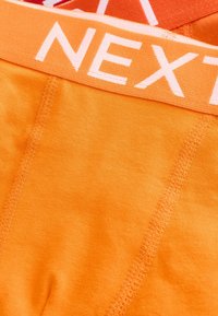Oranga underkläder med mjukt tyg, elastiskt midjeband med "NEXT"-logotyp i vitt och ren sömnad längs kanterna.