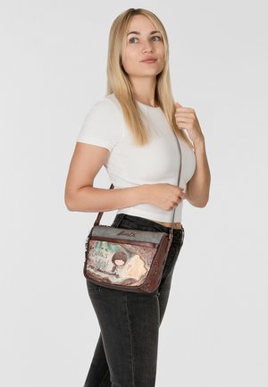 Sac à bandoulière en cuir marron avec un design graphique. Il possède une fermeture à rabat, des accents texturés et la phrase "La Terre est le Coeur."