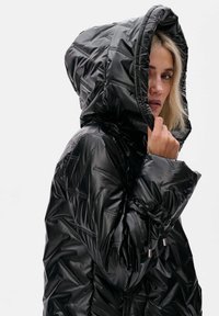 Zwarte pufferjack met een glanzende, gewatteerde textuur, voorzien van een capuchon, elastische manchetten en trekkoorddetails aan de onderkant.