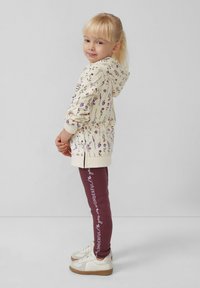 Lichtcreme hoodie met bloemenprint, gecombineerd met bordeauxrode leggings met witte tekst. Gecombineerd met witte sneakers met een gestructureerde zool.