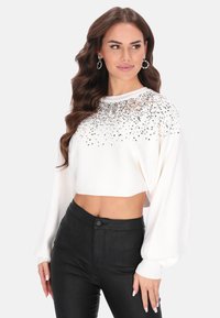 Witte cropped trui met geribbelde textuur, versierd met pailletten op de schouders, aangevuld met zwarte high-waisted broek.