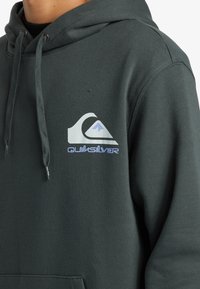 Felpa con cappuccio verde scuro realizzata in tessuto morbido, dotata di un logo Quiksilver bianco e blu sul petto e corde di regolazione sul cappuccio.
