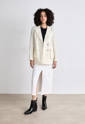 Kreemikaksiline bleiser, must topp, valge seelik külgslõikega ja läikivad mustad pahkluu saapad; sujuvad tekstuurid ja kohandatud disain.