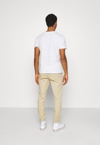 White cotton t-shirt with rolled sleeves, beige tapered pants, and white sneakers. Smooth texture, simple design, and muted colors.