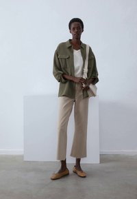Chemise boutonnée vert olive, haut blanc, pantalon cropped beige et ballerines marron. Les accessoires comprennent un sac léger. Design minimaliste, textures douces.