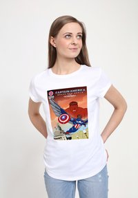Camiseta de algodón blanca con un colorido estampado de cómic de Capitán América con un escudo y un Hulk rojo de fondo, contra un suave cielo naranja.