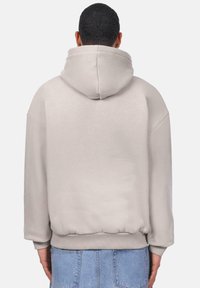 Hellgrauer Hoodie mit einer großen Kapuze, überschnittenen Schultern, gerippten Bündchen und Saum. Weicher Stoff mit keiner sichtbaren Musterung oder Hardware.