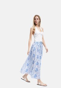 Witte haltertop van textuurstof, gecombineerd met een vloeiende maxi rok met blauw-witte bloemenprint. Strappy sandalen maken de outfit compleet.