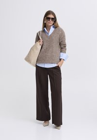 Brūns džemperis ar V veida izgriezumu, gaiši zila krekls zem tā, plašas brūnas bikses, bēša soma un neitrālas krāsas augstpapēžu kurpes; papildināts ar saulesbrillēm un auskariem.