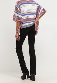 Poncho multicolore con strisce blu, rosse e bianche; presenta bordi frangiati e una vestibilità ampia. Abbinato a jeans neri svasati e tacchi.
