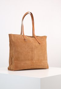 Bruine suède tote bag met twee leren handvatten, met een eenvoudig ontwerp en een gladde textuur, ideaal voor dagelijks gebruik.