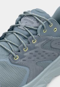 Chaussure de sport grise en maille et daim. Dispose d'une surface texturée, de lacets jaunes contrastants et d'un talon renforcé.