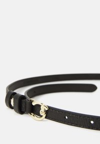Zwarte leren riem met een smal ontwerp, voorzien van een gouden gesp en een lus. Glad materiaal met meerdere verstelgaten.