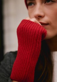 Gants sans doigts rouges côtelés en laine douce, offrant une coupe ajustée et un tissu texturé. Gros plan mettant en valeur la couleur vive et le motif.