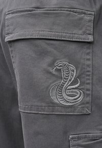 Γκρι παντελόνι φόρμας εργασίας με λεπτομερή γκρι κεντητό σχέδιο φιδιού στην κάτω τσέπη, με καθαρή ραφή και κλασική σιλουέτα φόρμας εργασίας.